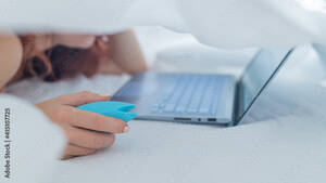 Girl Vibrator Porn - A woman lies in bed holding a clitoral vibrator and watching porn on a  laptop. The girl has sex online Stock Photo | Adobe Stock