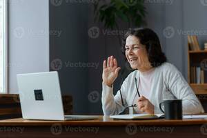 mature web cam videos - Happy mature blonde lady sitting on couch, holding video call with friends,  head shot close up portrait. Web cam view laughing middle aged woman having  fun, talking with grown up children online.